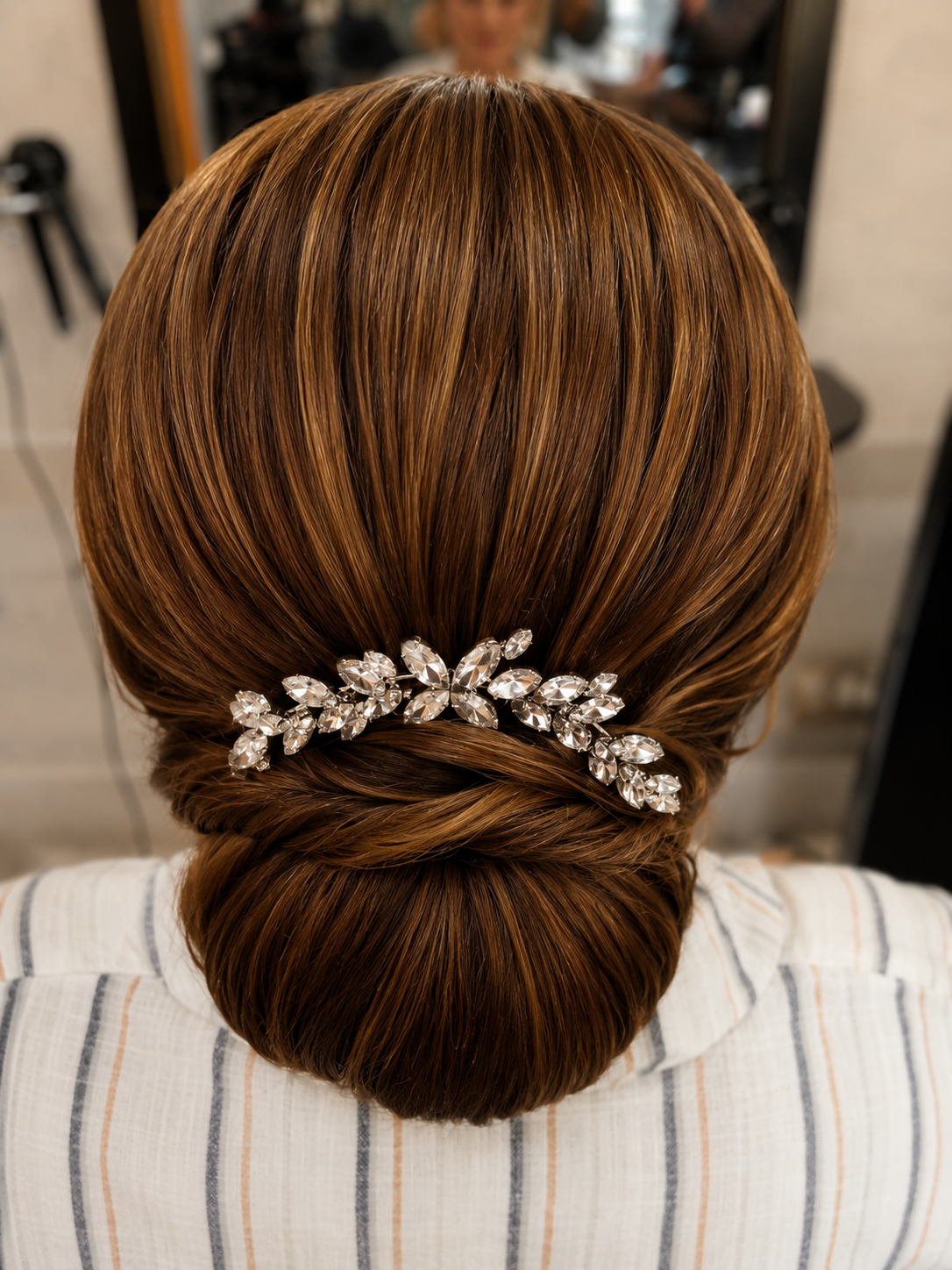 Sleek low chignon on caramel-highlighted brunette hair with crystal leaf comb